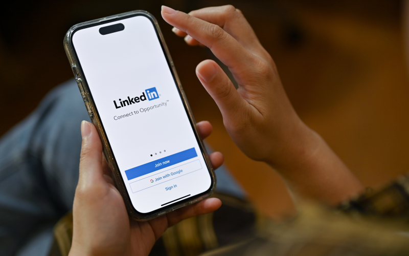 Professional holding a mobile phone with LinkedIn app open, preparing to send a personalised message to a potential client as part of their digital selling strategy.